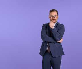 Handsome young professional manager touching chin and folding hand while posing against blue...