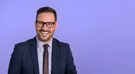Portrait of handsome cheerful male professional chief wearing eyeglasses and elegant suit looking at camera. Happy businessman smiling cheerfully and posing against isolated blue background