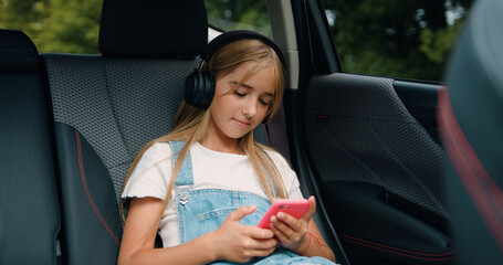 Beautiful elementary age girl passenger smiling and travels by car sitting in back seat and looks out open window. Family enjoy outdoor lifestyle travel together