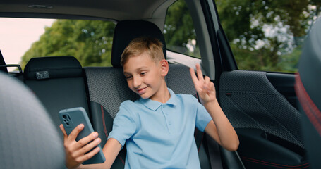 Child sitting in car and using smart phone and headphones. Attaractive little boy listing to music sitting in the back seat of a car during a family trip.