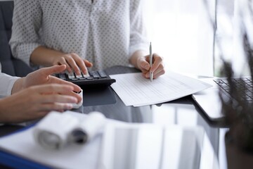 Woman accountant using a calculator and laptop computer while counting and discussing taxes with a client. Business audit concepts.