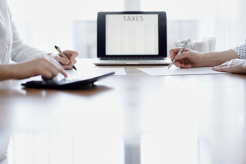 Two accountants using a laptop computer and calculator while counting taxes at wooden desk in office. Teamwork in business audit and finance.