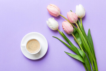 Spring background with flowers, a cup of coffee and a bouquet of pink and white tulips on colored table background with place for text. Copy space top view