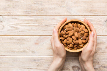 Woman hands holding a wooden bowl with almond nuts. Healthy food and snack. Vegetarian snacks of different nuts