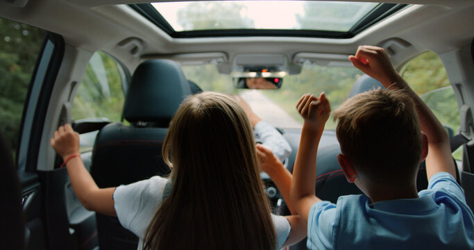 Two Little Boy And Girl Listens Enjoys Music And Dancing While Road Trip. Children Are Playing In The Car. Concept Of Journey.