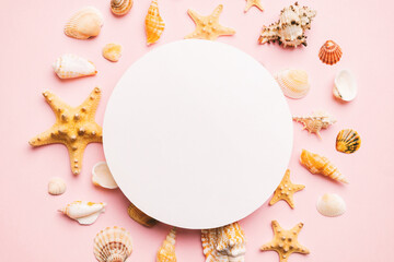 Summer time concept with blank greeting card and blank white paper on colored background. Seashells from ocean shore in the shape of frame separated with space for text top view