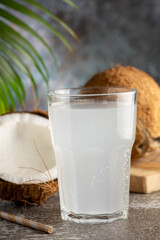 Glass with fresh coconut water and coconuts on the table.