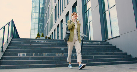 Young caucasian businesswoman came out of an office building, walking down the stairs and happy...