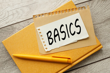 BASICS text on torn paper on yellow notebook light wooden background.