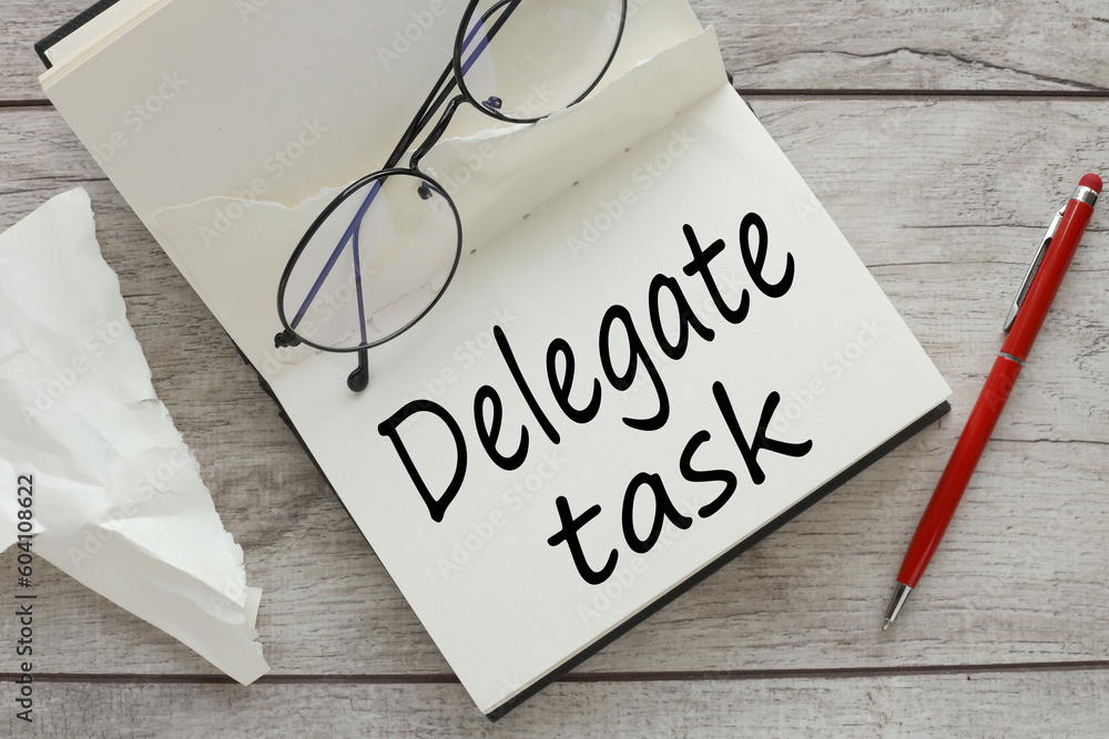 Poster glasses and a red pen. delegate tasks text on an open notebook