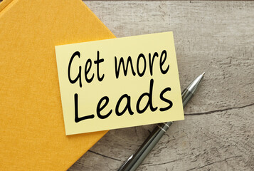 Get more leads! yellow sticker on a yellow notebook. on a wooden table