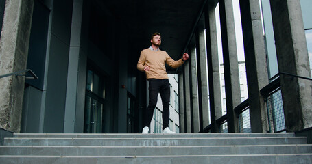 Happy and handsome caucasian young bearded businessman standing on the steps while leaving office...