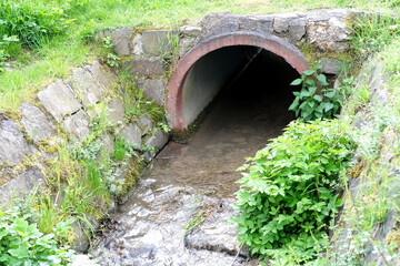 close-up concrete semicircular arch of a water drain well, a stream flows into a canal, sewage drains, the concept of a drainage system in Europe, a river drainage