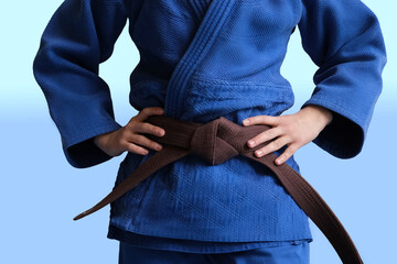 Judo girl with brown belt. A judoka teenager fighter poses in a blue kimono on a plain background....