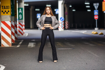 Fototapeta premium beautiful young girl with sunglasses in jacket posing near a modern office building with mirrored walls in a parking lot with road signs