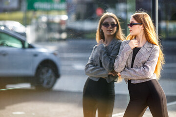 beautiful young girl with sunglasses in jacket posing near a modern office building with mirrored walls in a parking lot with road signs