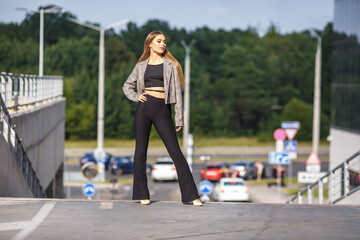 beautiful young girl with sunglasses in jacket posing near a modern office building with mirrored walls in a parking lot with road signs