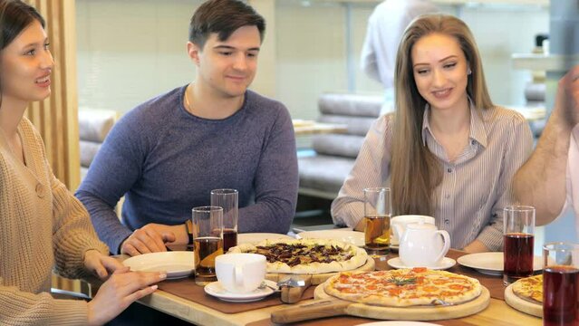 A happy group of friends are sitting at a table in a cozy restaurant, laughing and having fun. A group of girls and guys are laughing, enjoying a fast food lunch, pizza during a meeting.Pizzeria