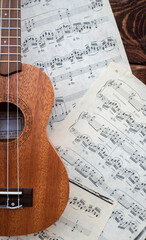 Ukulele guitar on music sheets on wooden background closeup