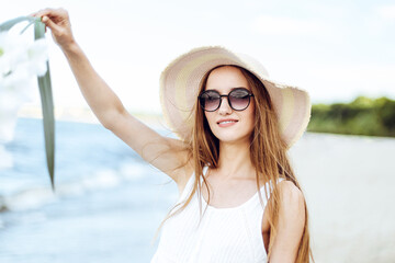Happy smiling woman in free happiness bliss on ocean beach standing with hat, sunglasses, and white...