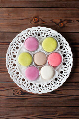 Colorful macaroons on white plateon wooden background, flatlay. Delicious almond meringue cookies. Copy space.