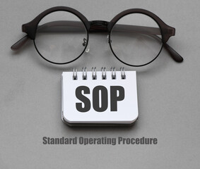 SOP Standard Operating Procedure words in notebook and gray sheet of paper.