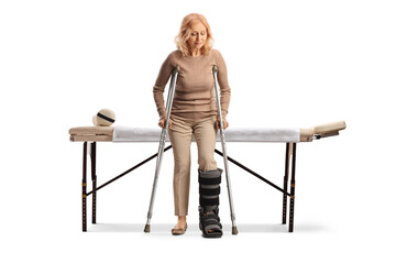 Woman in front of a medical table with a walking brace and neck collar trying to walk with a crutch