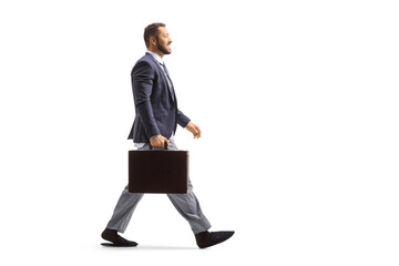 Full length profile shot of a man wearing a suit and bottom pajamas and walking with a briefcase
