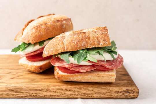 Italian sandwich with baguette, mozzarella, salami and arugula. Picnic sandwich on wooden board close up view - Powered by Adobe