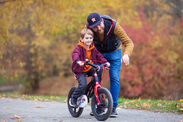 Obraz premium Father teaching his little son to ride bicycle in park. Bearded man helping child to learn bike. Family values, child support, fathers day concept. Selective focus.