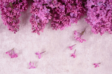 Beautiful spring lilac flowers background. Floral frame made of purple lilac branches on light pink table. Mock up greeting card with empty place for text