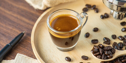 cup of hot Intense coffee dark shot in glass on wooden table with beans with crema. coffee beans and cup full of Intense dark shot coffee in glass cup