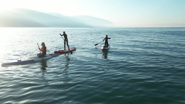 a company of SUP surfers are sailing on a board with an oar in the sea at dawn against a beautiful background of calm water