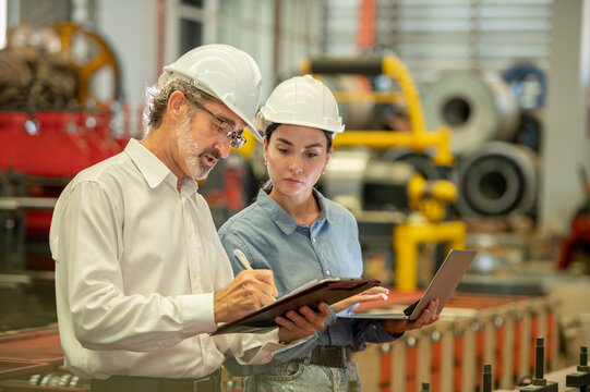 Two engineer technician assistant checker inspect checking walk heavy machine construction installation in factory . Boss and secretary talking and check inventory in clipboard maintenance factory