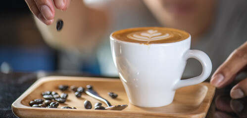 White ceramic cups of cappuccino with latte art Barista make coffee by pouring spills hot milk cream on black coffee. Barista serve holding cup of hot latte and coffee beans on wooden table cafe shop