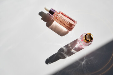 Cosmetic product bottles with rose petals and hard shadow. Skincare beauty product concept - obrazy, fototapety, plakaty