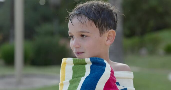 Young boy bundles up in beach towel after getting out of swimming pool in summer - close up on face