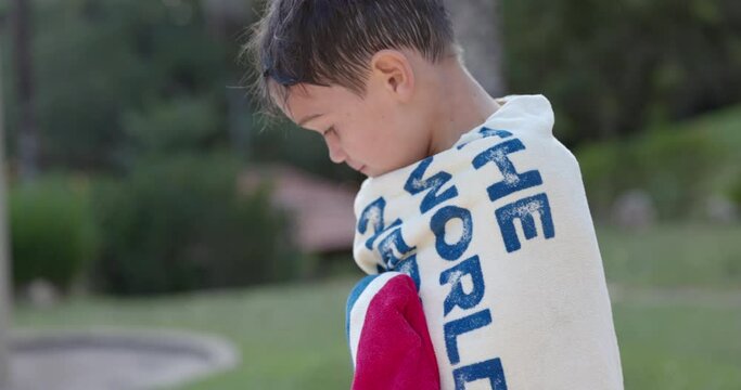 Young boy outside on sunny day wrapped in towel after swimming pool