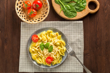 Pasta in cream sauce with cheese garnished with spinach with fork next to tomatoes, knife and greens.