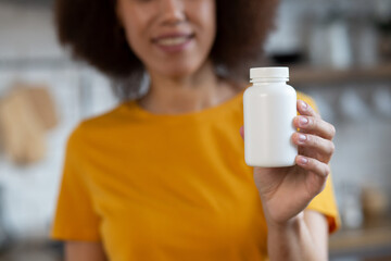 Happy young smiling African American woman holding bottle of dietary supplements or vitamins in...