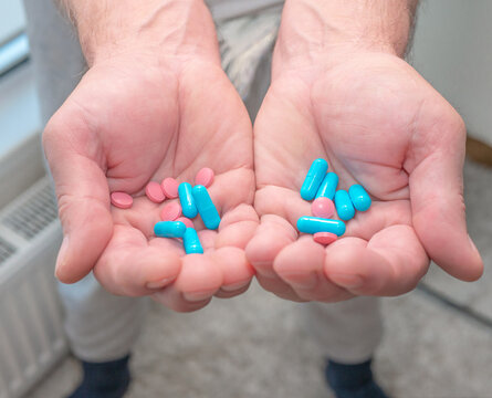 An elderly man has pills in his hands. The concept of treatment with pills prescribed by a doctor. Demonstration of blue healing capsules. Vitamins for the elderly.