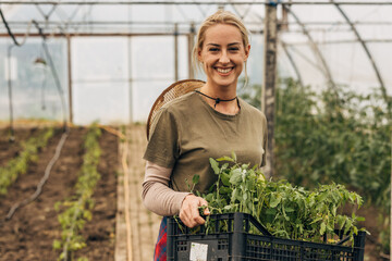Happy woman carrying a crate with seedlings and looking at the camera.