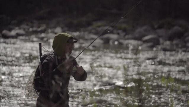 Pescatore  in azione durante una battuta di pesca a spinning. Pescare su un torrente montano in Trentino, Italia.