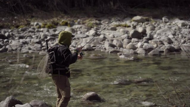 Pescatore  in azione durante una battuta di pesca a spinning. Pescare su un torrente montano in Trentino, Italia.