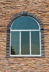 Beautiful arched window in building, view from outdoors. White painted wood arched window in a red stone wall