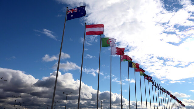 Low angle view of multiple flags on poles over blue sky with clouds background