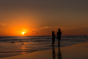 Couple holding hands while walking along the seashore on the beach at sunset.