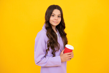 Child with coffee or tea cup isolated on yellow studio background. Teenage girl with take away beverage. Happy face, positive and smiling emotions of teenager girl.