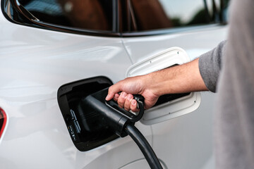 Person plugging in a charging cable to a white car at a electric vehicle fast charging station, closeup. Renewable energy. The sustainable future of transportation.