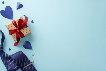 A top-down view of hearts, accessories, blue necktie with clip, and craft paper gift box with...